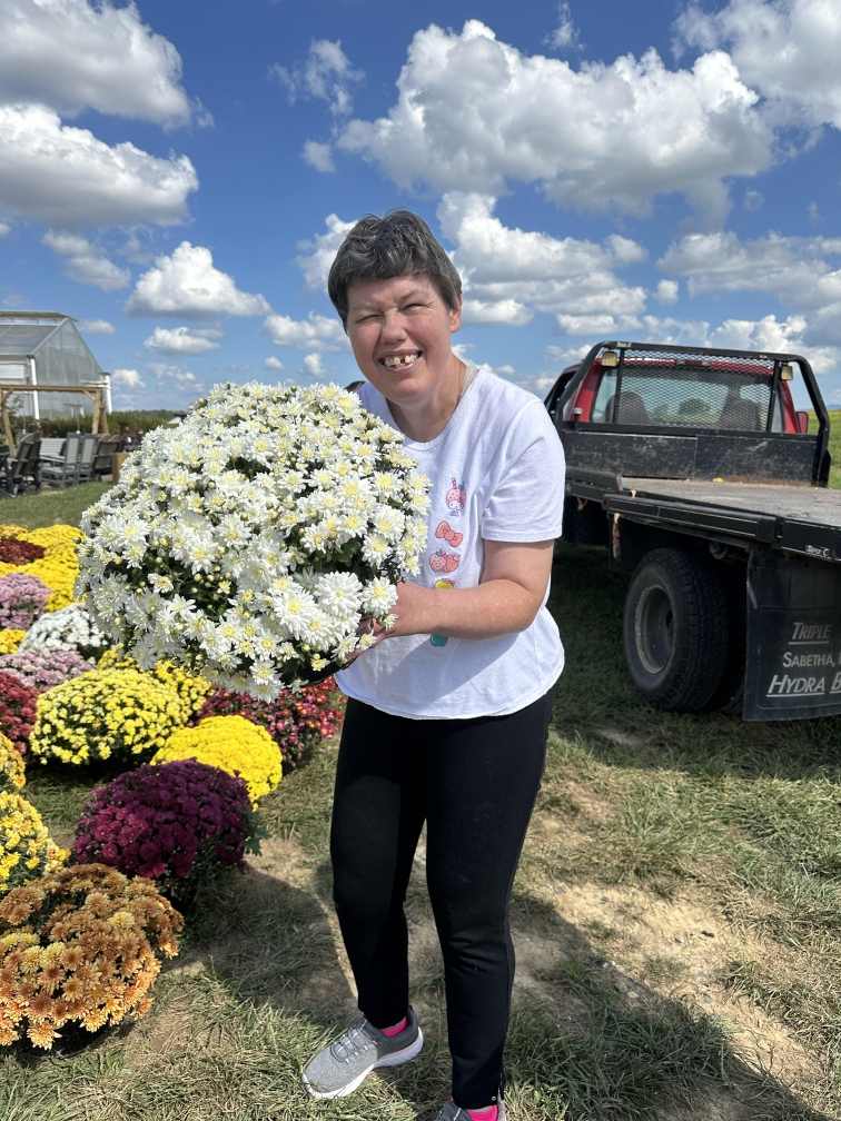 Woman, outside under a blue sky, holding white mums