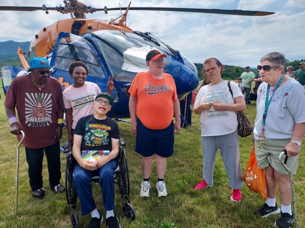 Group of 5 people from Pleasant View standing and one person sitting in a wheelchair in front of a helicopter.