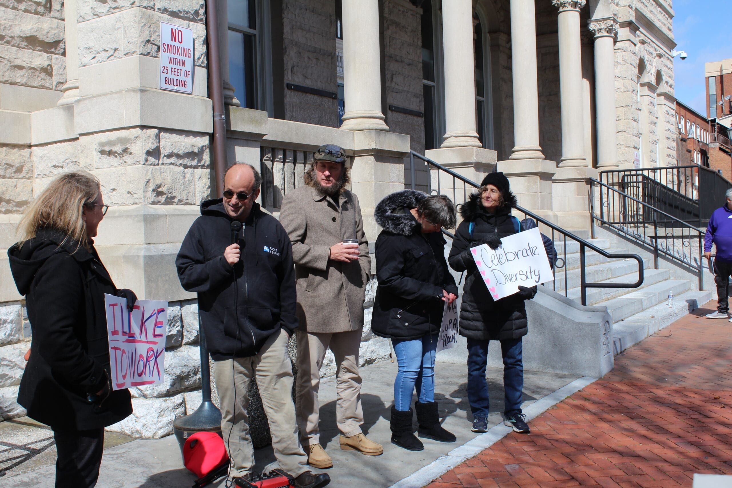 a group of 5 people standing in front of the Rockingham County Court House. One man is speaking in a microphone.