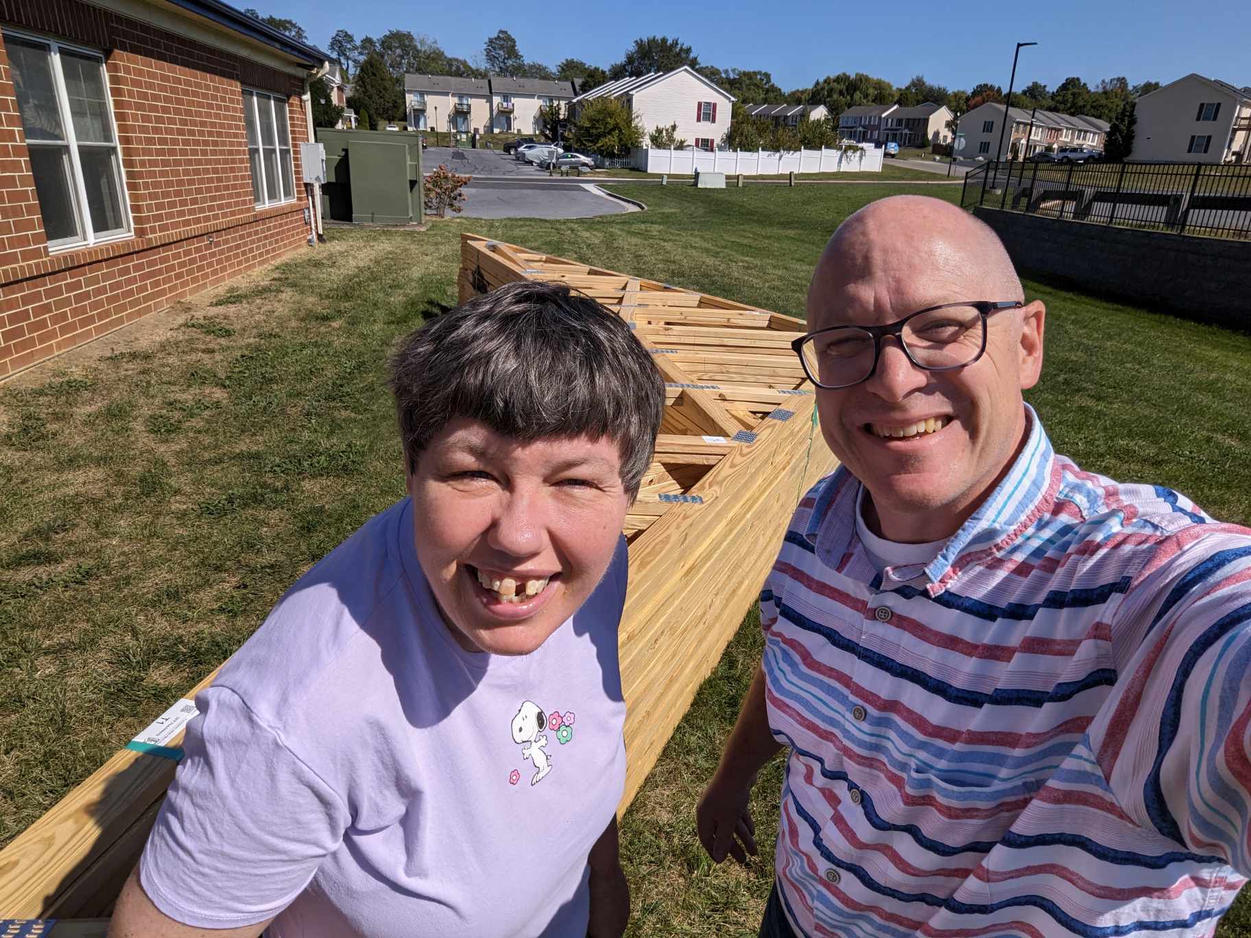 A woman and a man smile as they take a selfie in front of construction materials