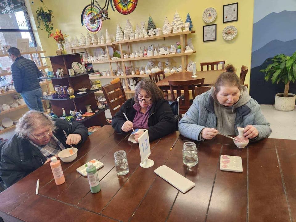 Three women are seated at a table painting projects at You Made It.