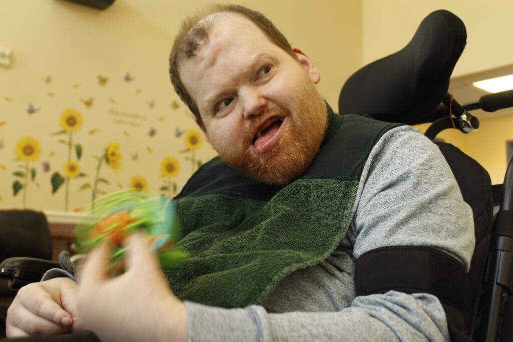 Billy smiles while you see his hand blurred. He is holding a musical instrument and shaking it.