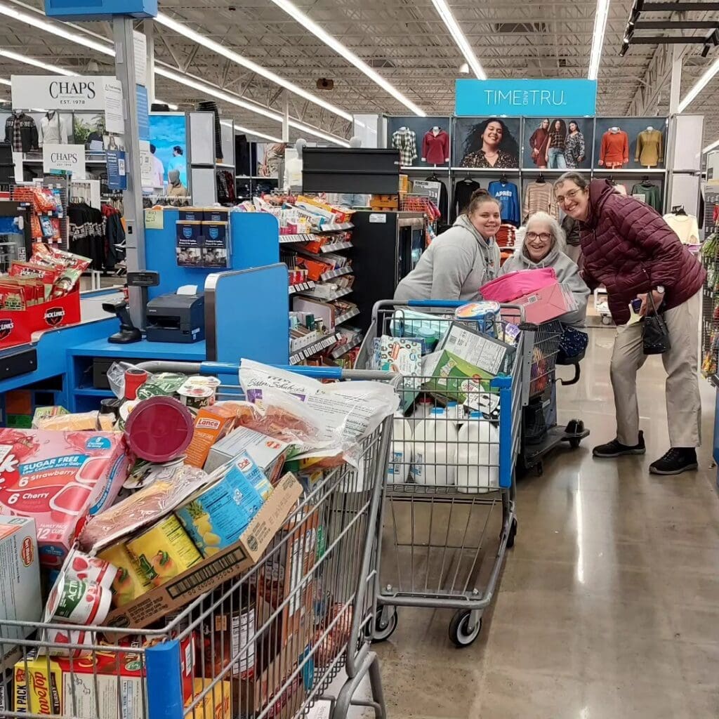 A woman in motorized shopping cart and 2 support staff with another shopping cart in front.
